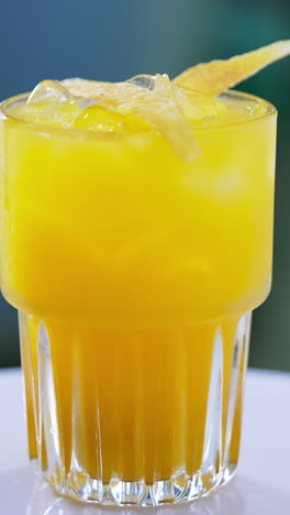 orange tasty cocktail decorated with ice cubes and chips. beautiful beverage on the spinning table close up. vertical video