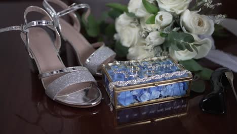 close up of bridal accessories including silver heels, white bouquet, and ring box on a table