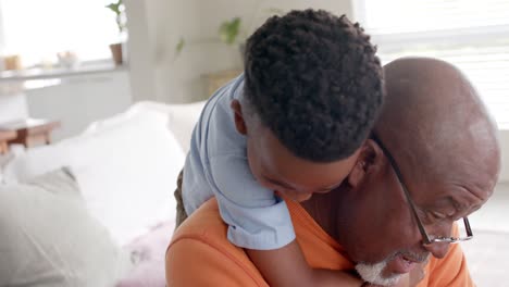 Happy-african-american-grandson-and-grandfather-embracing-and-smiling-on-couch-at-home,-slow-motion