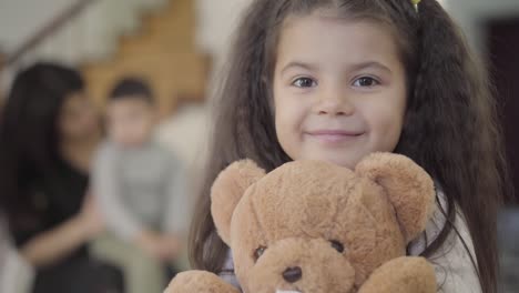 close-up of a happy middle eastern girl with brown eyes and curly hair holding the teddy bear and smiling