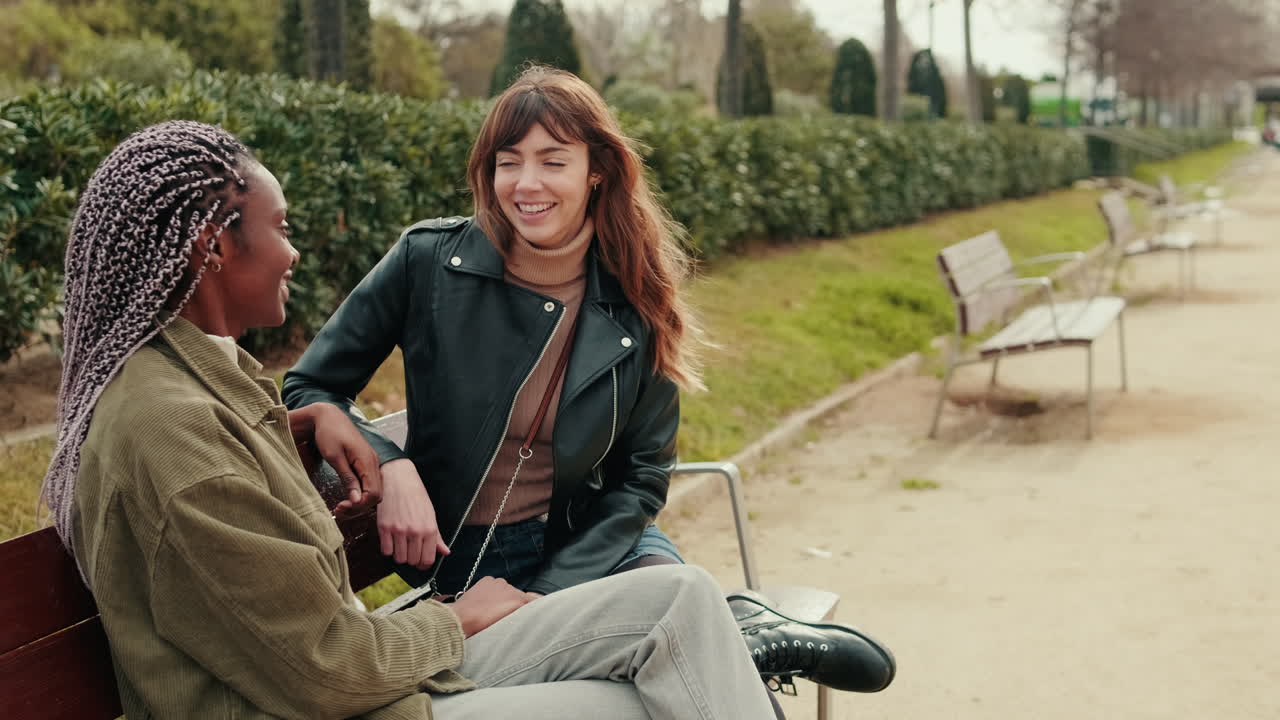 Two Young Women Talking and Laughing on a Park Bench