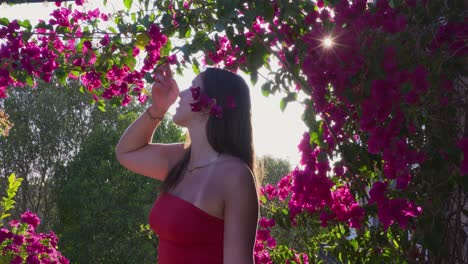 a young girl with flowers in her long black hair looks at the blossoms of a bush