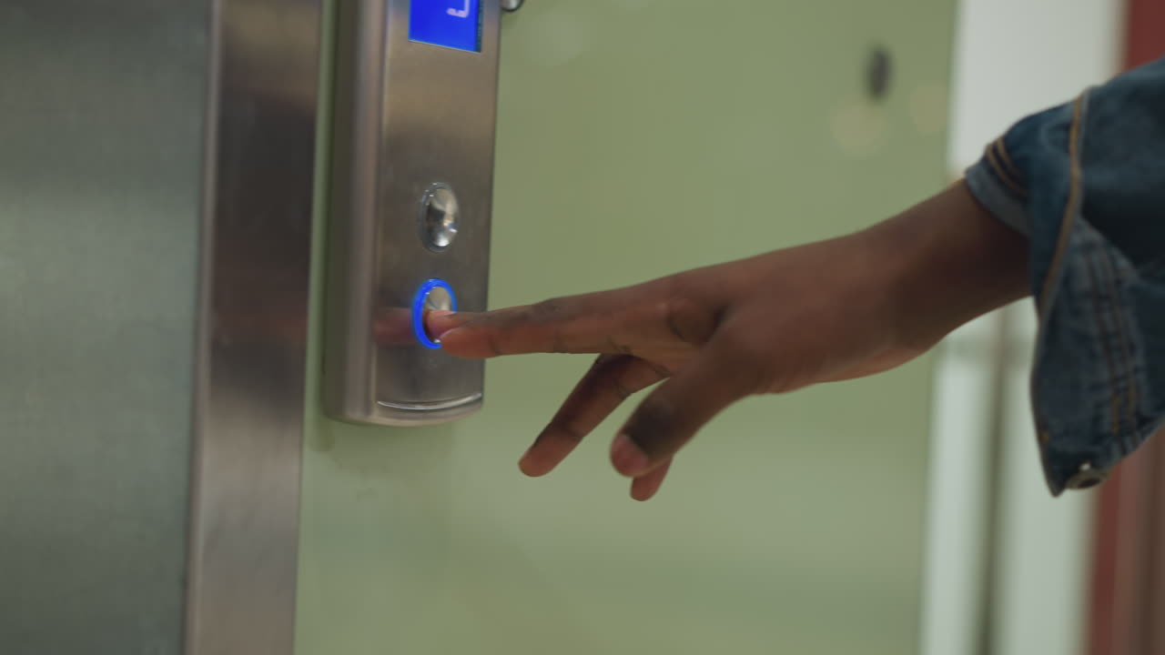 Close-up shot of finger pressing elevator button, illuminated blue arrow pointing upwards. Modern control panel with metallic design, green wall, indicating movement to upper floor