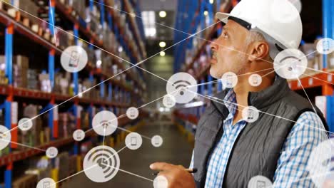 Animation-of-network-of-icons-over-caucasian-male-senior-supervisor-checking-stock-at-warehouse