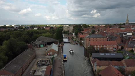 a drone video of a river boat heading towards newark town lock. the footage lowers down and captures the building around including g newark castle and st mary cathedral.
