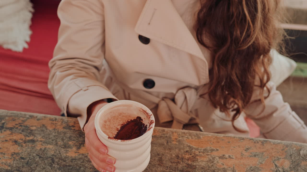 Woman's hand holding a cup of hot chocolate, with cocoa powder visible on top