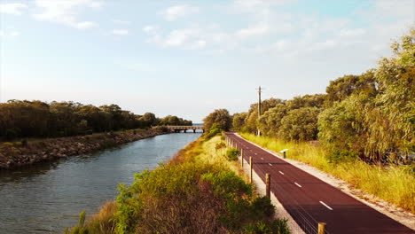 Bird's-eye-drone-flying-over-riverside-cycle-path-in-wild-wetlands-in-western-Australia