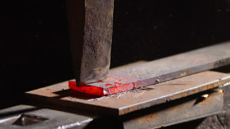 blacksmith hits chisel into red-hot piece of metal to split it, close-up