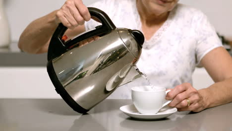 mujer vertiendo agua caliente de la tetera en la taza