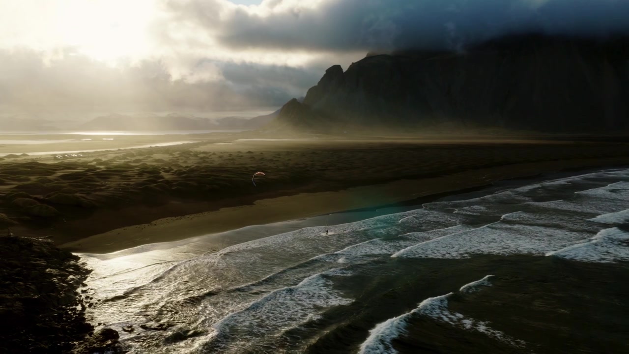 Stokksnes black sand beach, Atlantic surf, wet reflective shoreline, sea mist, Vestrahorn cliffs and dramatic clouds beneath low sunlight, southeast Iceland, drone slide.