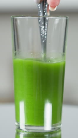 primer plano de una cuchara mezclando jugo de verduras verde vibrante en un vaso alto transparente, mezclando un jugo verde fresco con una cuchara en un vidrio alto, iluminación natural