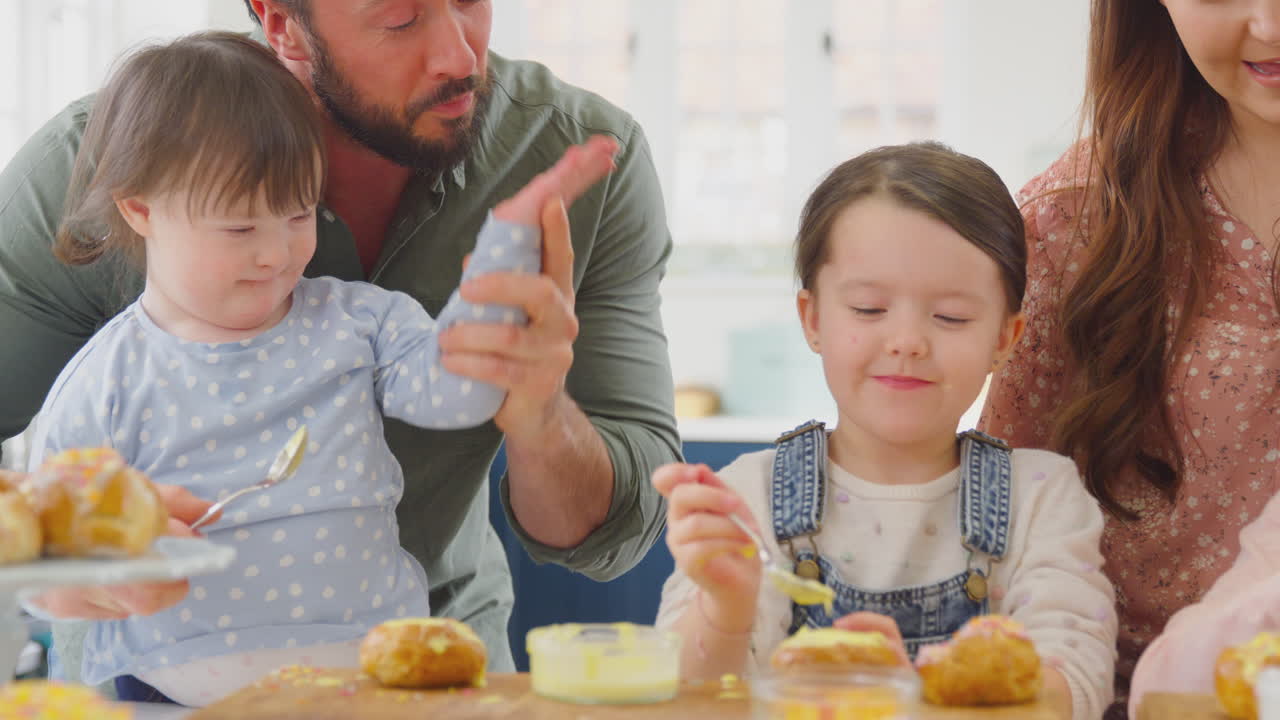 다운 증후군을 가진 가족 딸은 집에서 테이블 주위에 앉아 케이크를 고 장식합니다.