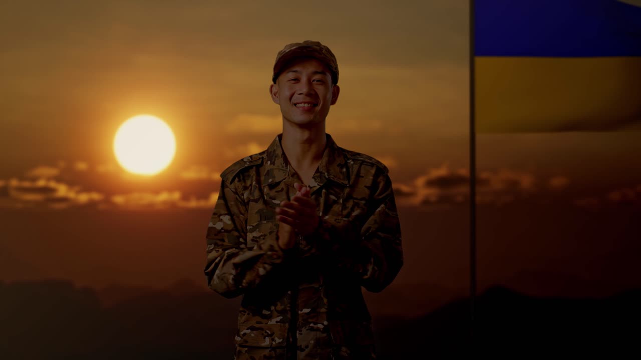 해가 지는 동안 우크라이나 국기 앞에서 박수를 치는 미소 짓는 군인