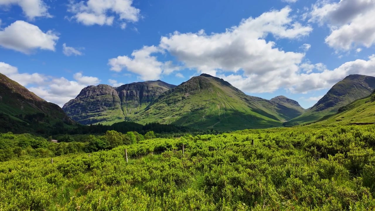 Splendido paesaggio verde nelle Highlands scozzesi con campi verdi e grandi montagne, nuvole fluttuano nel cielo blu in una soleggiata giornata estiva a Glencoe, Scozia
