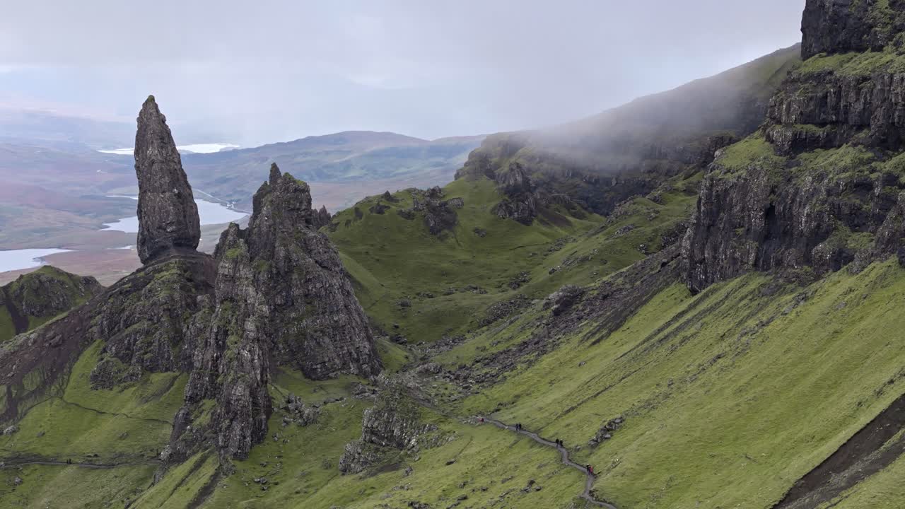 Circling left aerial view of Old Man of Storr with vibrant green landscape and low fog