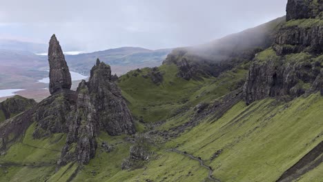 circling left aerial view of old man of storr with vibrant green landscape and low fog