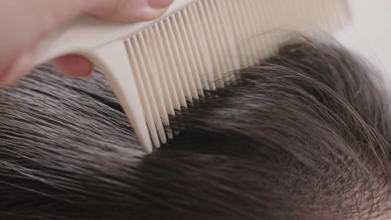 バスルームで、白い櫛を使って頭皮をとかし、生え際を整えている手。
