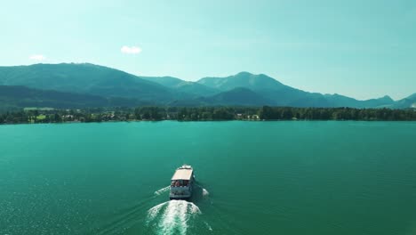 drone follows and then flies by a boat moving across the turquoise waters of wolfgangsee lake