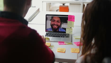 hombre barbudo sonriente hablando con sus colegas a través de una computadora portátil.