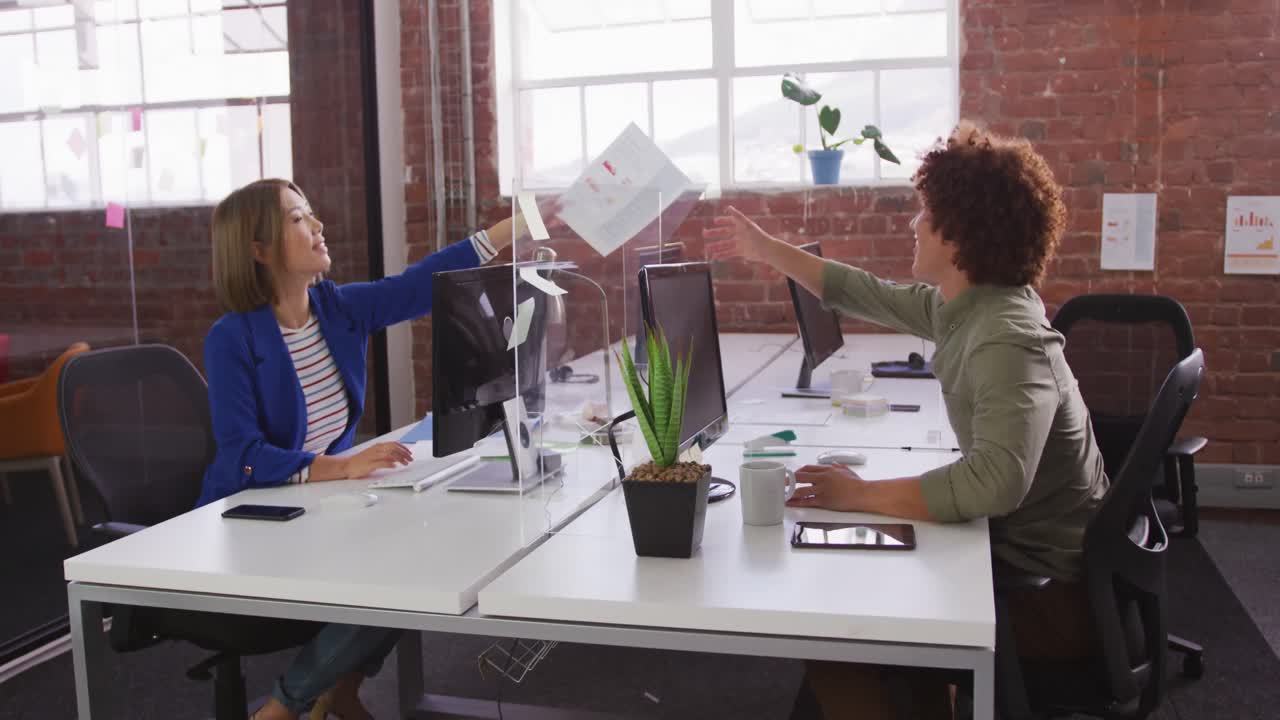 diversos colegas masculinos y femeninos en el trabajo intercambiando documentos a través de un guardia contra estornudos