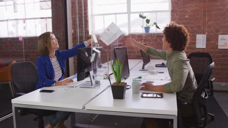 diversos colegas masculinos y femeninos en el trabajo intercambiando documentos a través de un guardia contra estornudos
