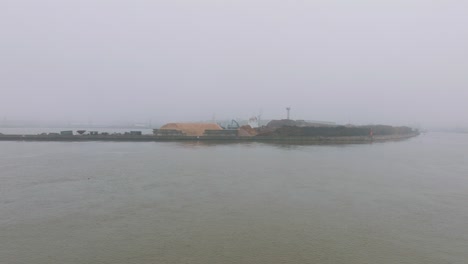 Luftaufnahme-Des-Holzterminalkrans,-Der-Holz-In-Das-Frachtschiff-Verlädt,-Hafen-Von-Liepaja,-Holzholzexport,-Bewölkter-Tag-Mit-Nebel-Und-Dunst,-Weiträumige-Drohnenaufnahme,-Die-Sich-Vorwärts-Bewegt