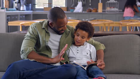 father and son sitting on sofa looking at counting book together