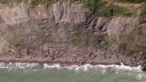 Top-view-of-cliffs-next-to-ocean-waves,-very-small-human-walking