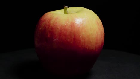 manzana fuji giratoria con gotas de agua sobre fondo negro aislado, primer plano