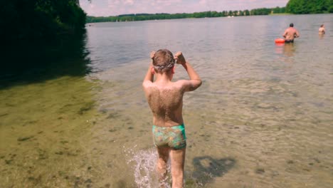 happy child boy sand on his body walking towards the lake water to swim