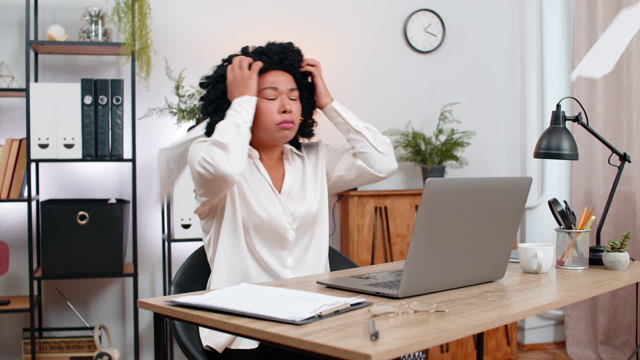Une femme d'affaires afro-américaine panique lorsque son ordinateur portable se fige et que des problèmes techniques l'obligent à restaurer rapidement des documents pour reprendre son travail