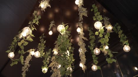 Hanging-globe-lights-with-greenery-and-white-flowers,-creating-a-whimsical-ceiling-decor