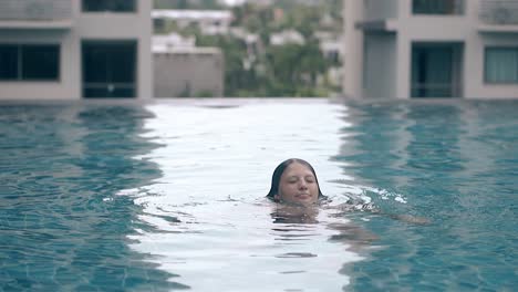 una señora sonriente emerge del agua en la piscina en cámara lenta
