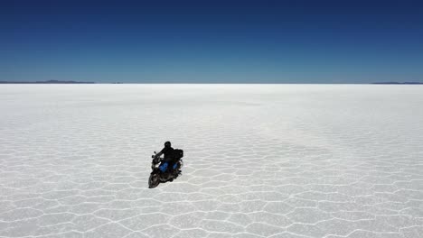 Person-on-motorcycle-rides-diagonally-from-horizon-on-vast-salt-flat