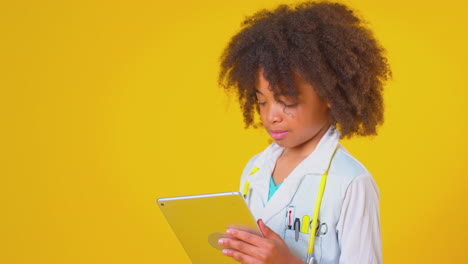 studio portrait of boy dressed as doctor or surgeon with digital tablet against yellow background