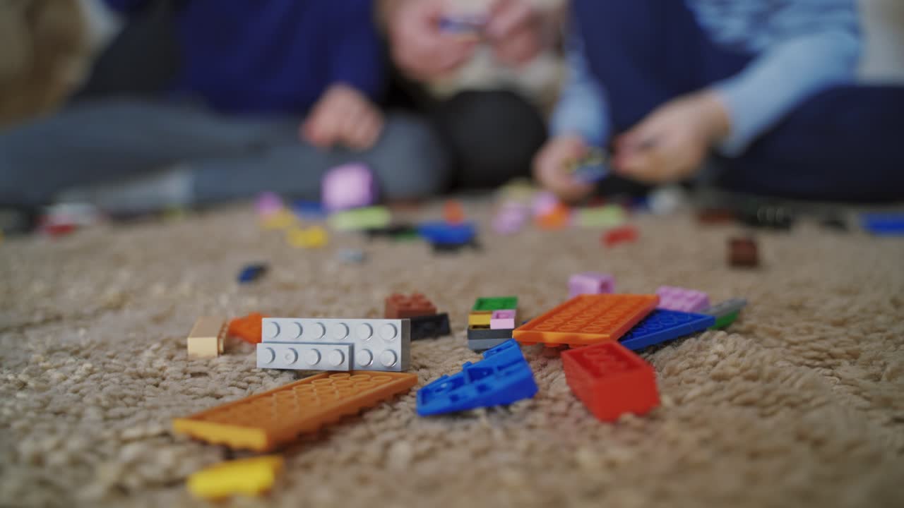 Blocks of constructor with different color and shape are on the carpet on the background of children and adults playing with it. Close-up. Blurred background.