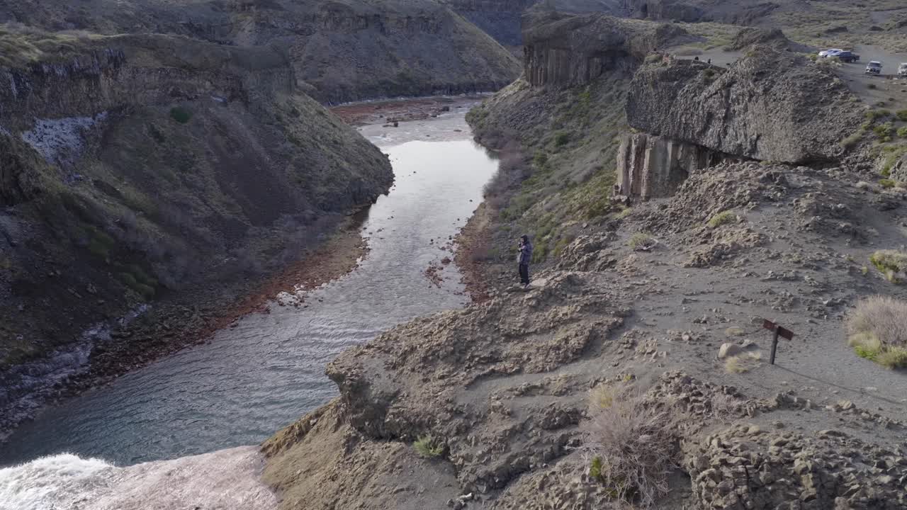 Man drinking mate on the edge of Salto del Agrio waterfall surrounded by rocky canyon landscape