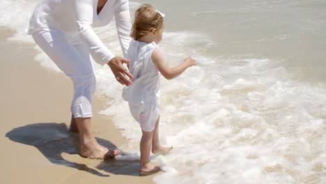 Mutter-Hält-Ihr-Mädchen-Am-Strand-Planschen-Wasser