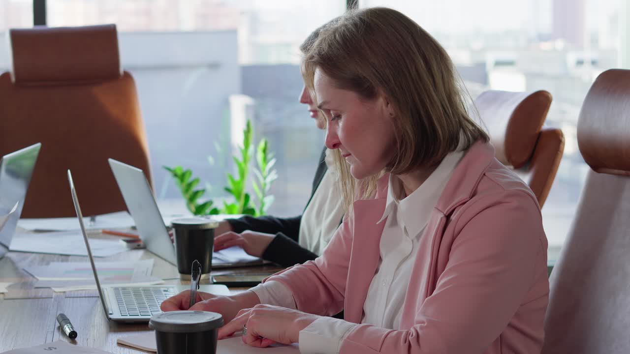 Close-up of a confident blonde girl with a bob hairstyle in a pink business suit sits at a table in the office during a business meeting of a businesswoman in a modern office