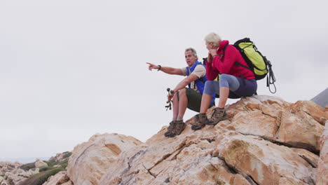 Älteres-Wanderpaar-Mit-Rucksack-Und-Trekkingstöcken,-Das-In-Eine-Richtung-Zeigt-Und-Sich-Unterhält