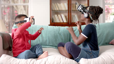 african american sister and brother using vr headset in living room, slow motion