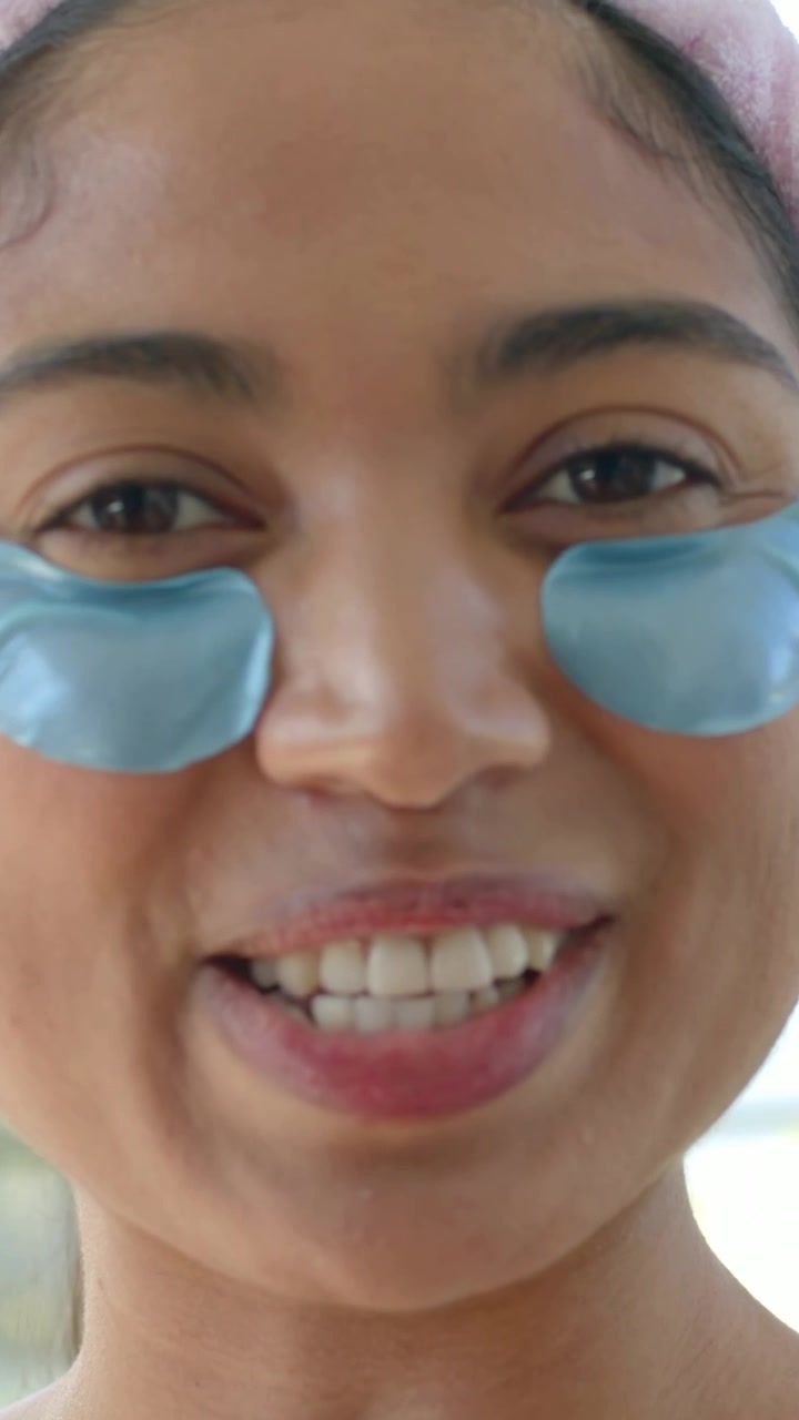 Video vertical: Primer plano de mujer con diadema rosa grabando un vlog en casa, mostrando parches azules para los ojos.