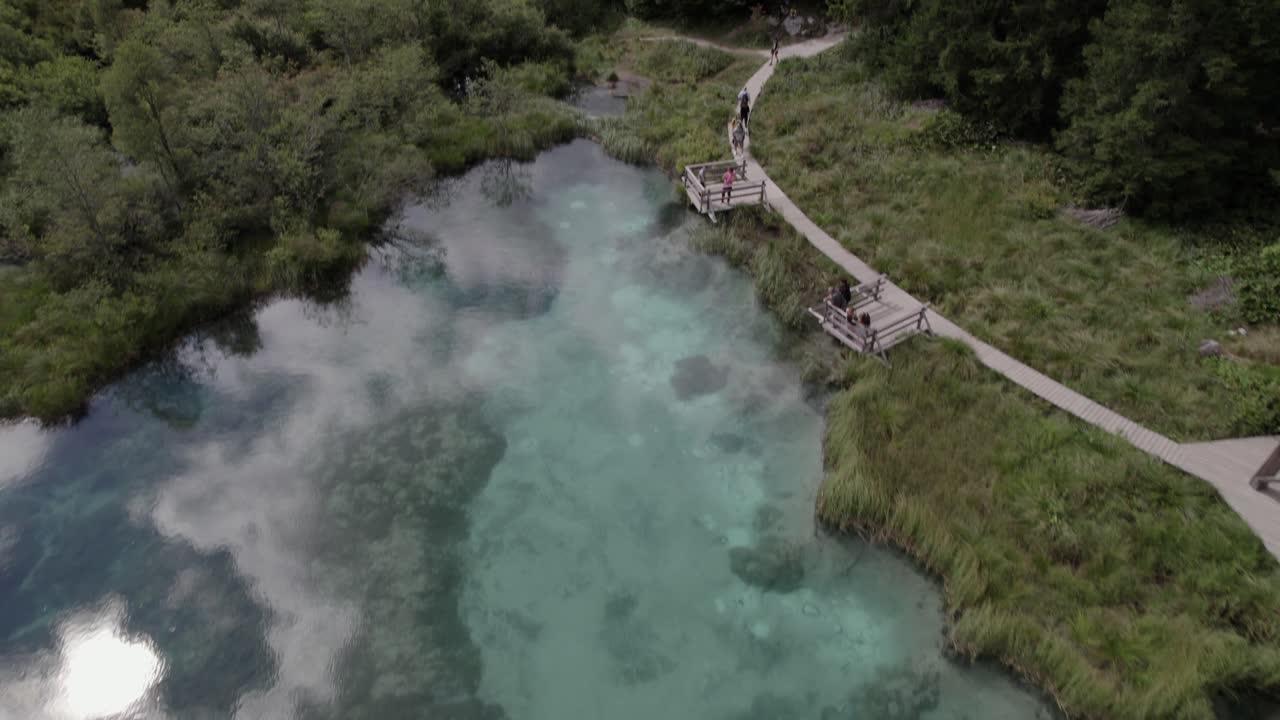 Beskrivande frontal drönarvideo av Savas källsjö i Zelenci naturreservat, med turister i Slovenien.