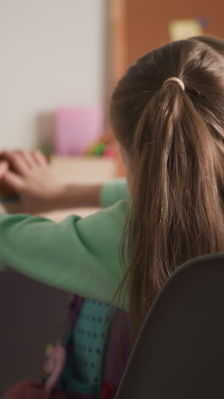 Cute girl with long ponytails takes books stack out of schoolbag sitting in room. Primary school pupil prepares for homework at home after classes