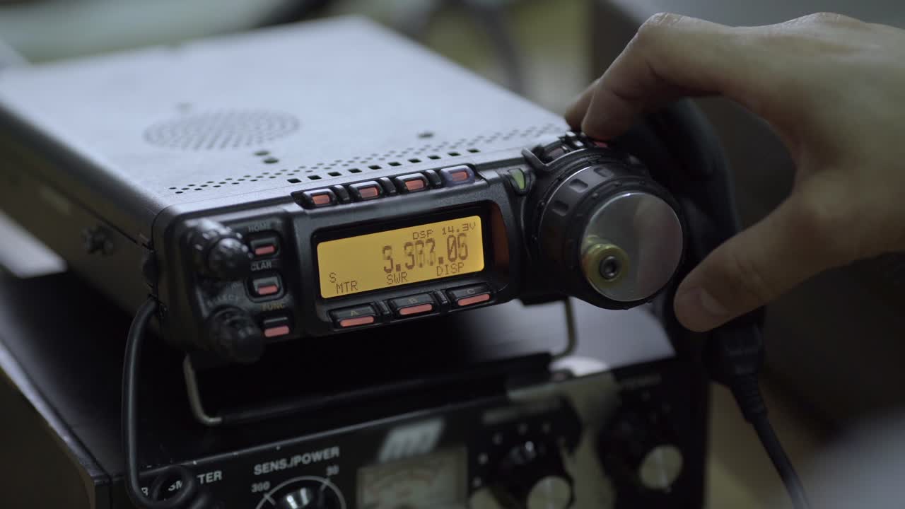 A hand precisely adjusts the dials and buttons of a Citizen Band (CB) radio. Focus on equipment.