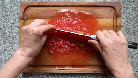 chopping tomatoes using a knife on wooden board to make tomato sauce