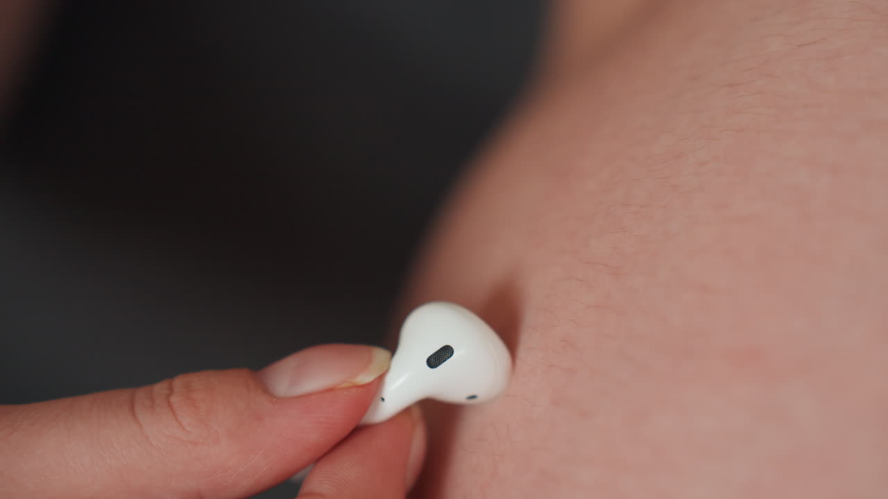 Pasangan menempelkan earbud ke perut hamil, momen mendengarkan prenatal yang intim dengan earbud putih di kulit hangat, pasangan berbagi musik dengan bayi yang belum lahir, adegan domestik yang taktil berfokus pada koneksi