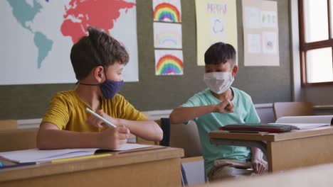 Two-boys-wearing-face-masks-greeting-each-other-by-touching-elbows-at-school