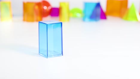 a hand interacts with colorful 3d geometric shapes on a white surface, highlighting educational and playful elements