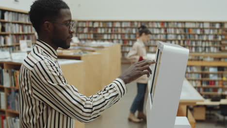 hombre negro usando pantalla digital interactiva en la biblioteca